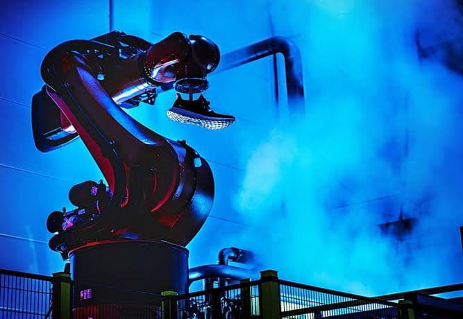 adidas Speedfactory — robotic manufacturing arm holding a finished sneaker, lit in deep blue